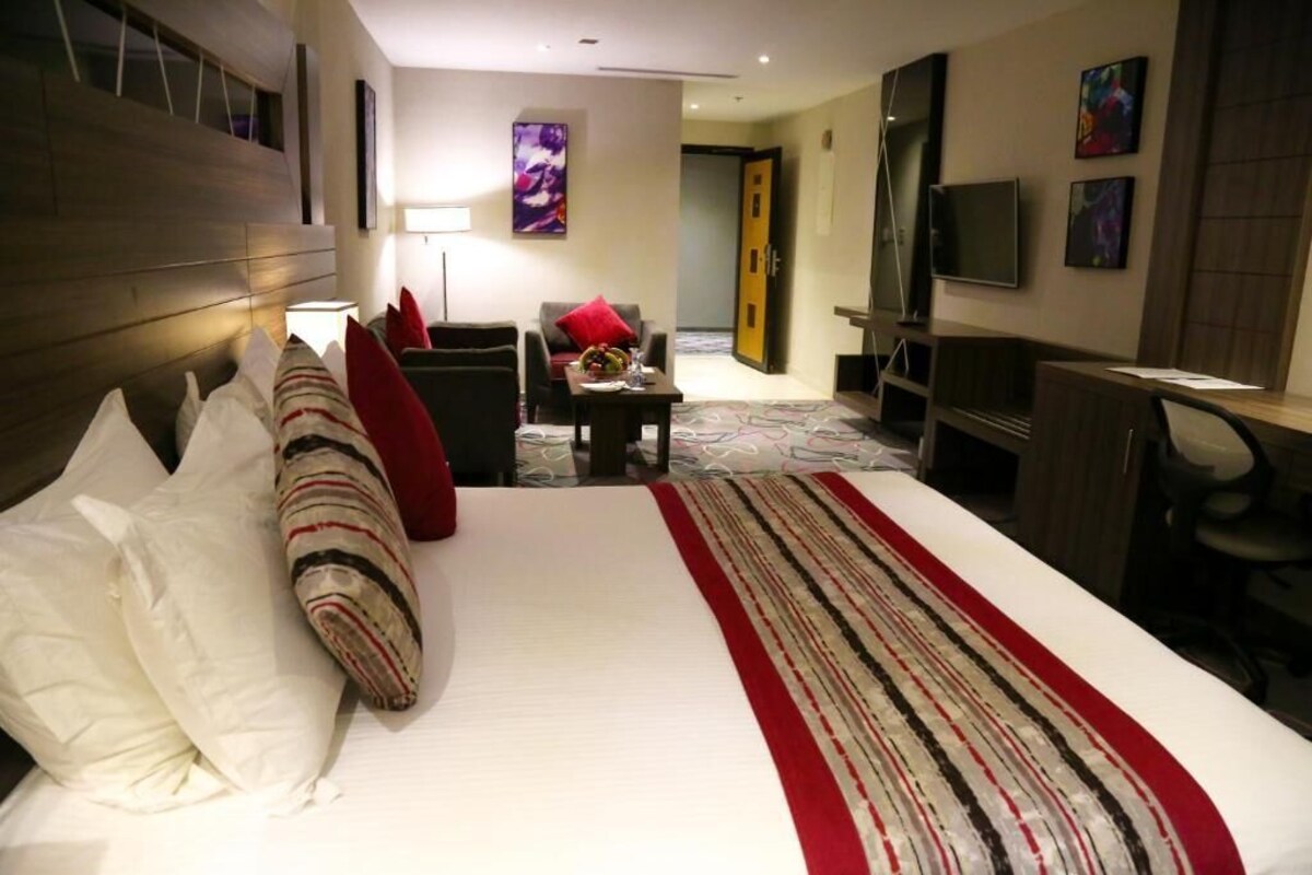A hotel room with a bed, a desk, a chair, a TV, and a door.