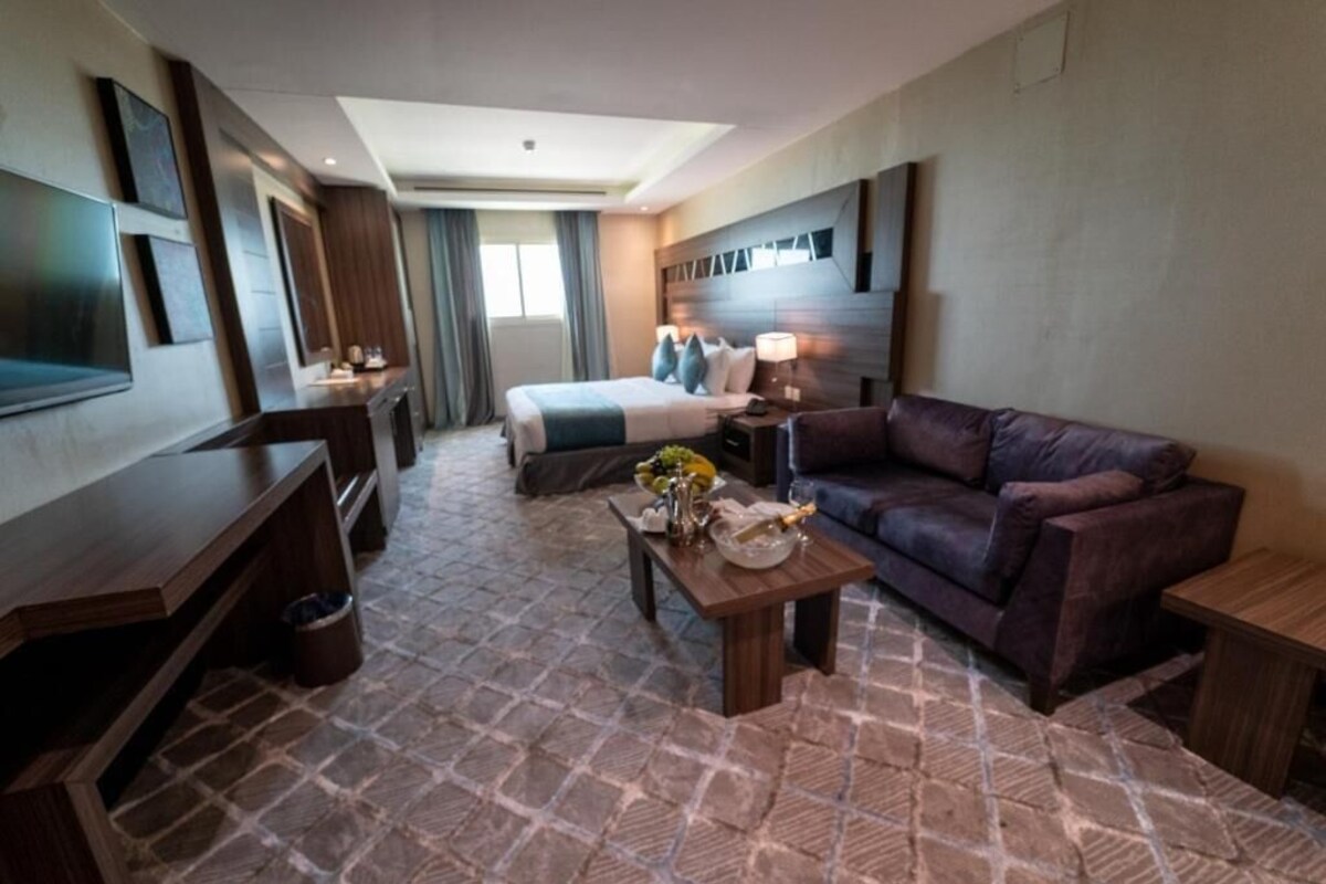 A hotel room with a bed, a sofa, a TV, a desk, and a coffee table.