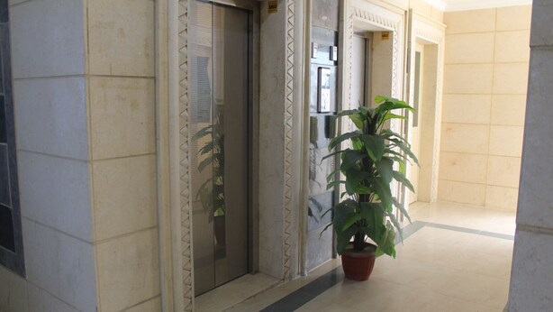 An interior corridor with tiled walls, two elevators, and a potted plant. - ماجيك سويت الرقعى Magic Suite ALRaggi (Kuwait City)