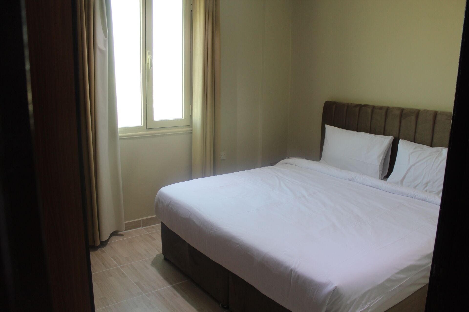 A bedroom with a bed, a window with curtains, and a wooden headboard.