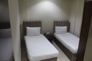 Una habitación de hotel pequeña y con una cama individual, con dos camas individuales, cada una con cabecero de madera y ropa de cama blanca.