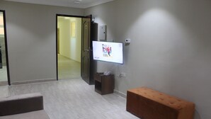 A modern hotel room with a flat-screen TV mounted on the wall, a wooden bench, and a tiled floor. - ماجيك سويت الرقعى Magic Suite ALRaggi (Kuwait City)