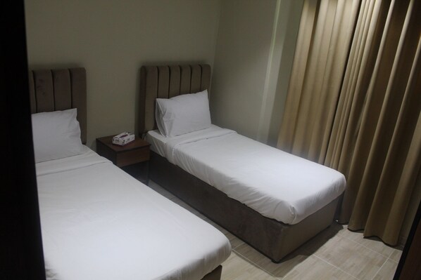 A hotel room with two single beds, a nightstand with a phone, and a curtain.