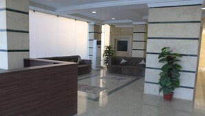 A reception area with a wooden reception desk, two sofas, a potted plant, and a tiled floor. - ماجيك سويت الرقعى Magic Suite ALRaggi (Kuwait City)