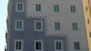 A multi-story building with a uniform facade, featuring a grid of windows and a patterned section at the bottom. - ماجيك سويت الرقعى Magic Suite ALRaggi (Kuwait City)