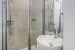 A modern bathroom with a glass-enclosed shower, a white sink, and a large mirror.