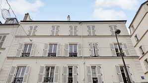 A multi-story building with white facades and shutters, featuring balconies with wrought iron railings. - Rue Lepic - quintessential winding cobblestone street- Take a step into the past (Paris)