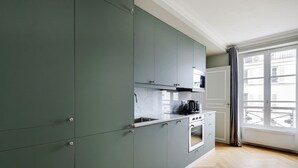 A modern kitchen with grey cabinets, a stove, and a window with a view of buildings. - Rue Lepic - quintessential winding cobblestone street- Take a step into the past (Paris)