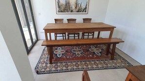 A dining area with a wooden table and benches, a patterned rug, and a painting on the wall. - Naiika Co Living (Denpasar)