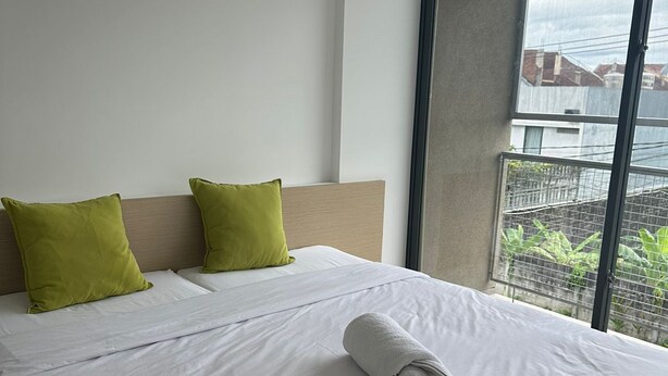 A hotel room with a bed, two green pillows, and a rolled white towel. - Naiika Co Living (Denpasar)