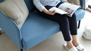 A person sitting on a blue sofa with a beige pillow, reading a magazine. - Naiika Co Living (Denpasar)
