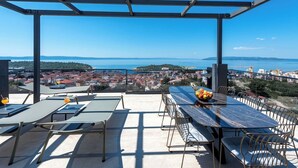 A rooftop terrace with a clear view of a coastal city, furnished with tables and chairs, and a bowl of fruit on the table. - villa Aurelia 2-amazing sea and city rooftop view (Makarska)