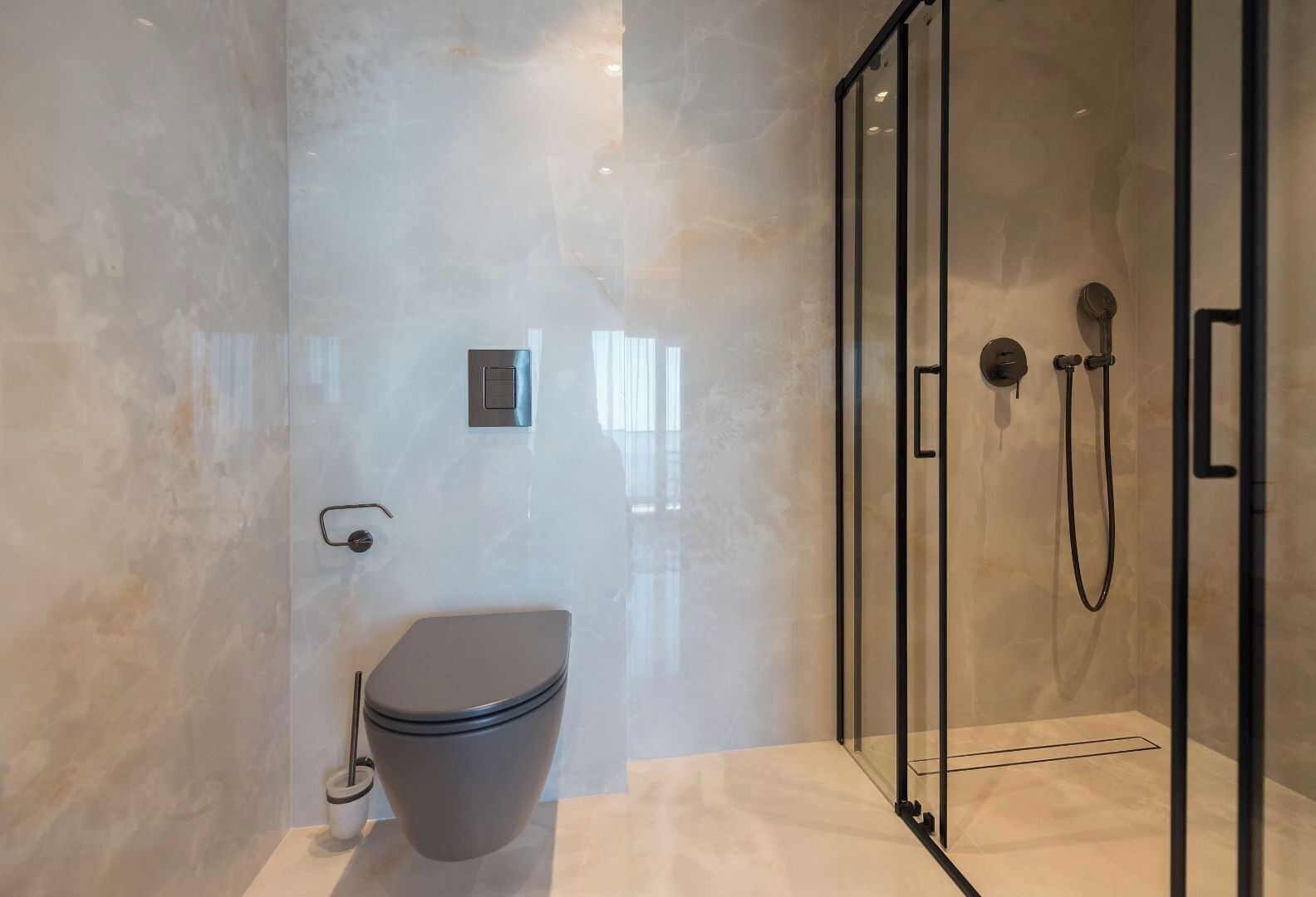 Une salle de bain moderne avec une douche à l’italienne, des toilettes et un mur en marbre.