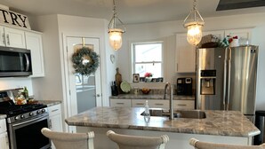 Una cocina moderna con una isla central, electrodomésticos de acero inoxidable e iluminación colgante.