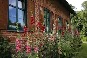 A brick building with multiple windows and a garden with various flowers.