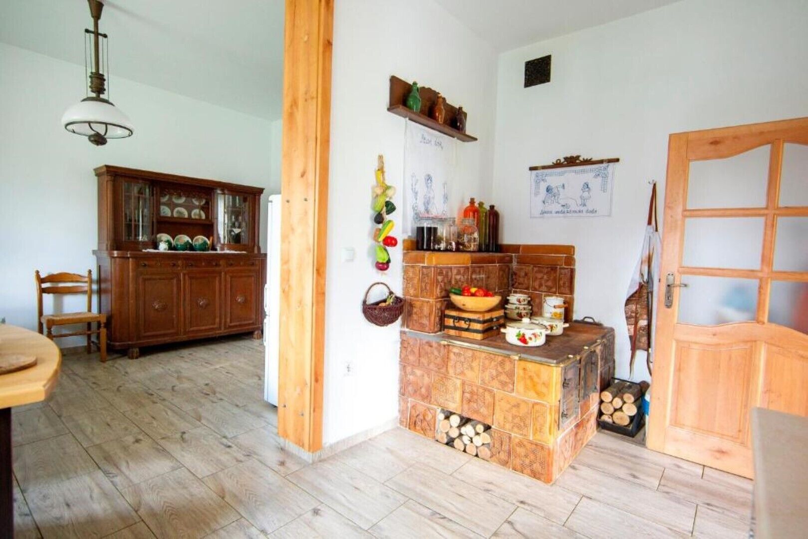 Une cuisine rustique avec un meuble en bois, un panier à fruits suspendu et un poêle carrelé.