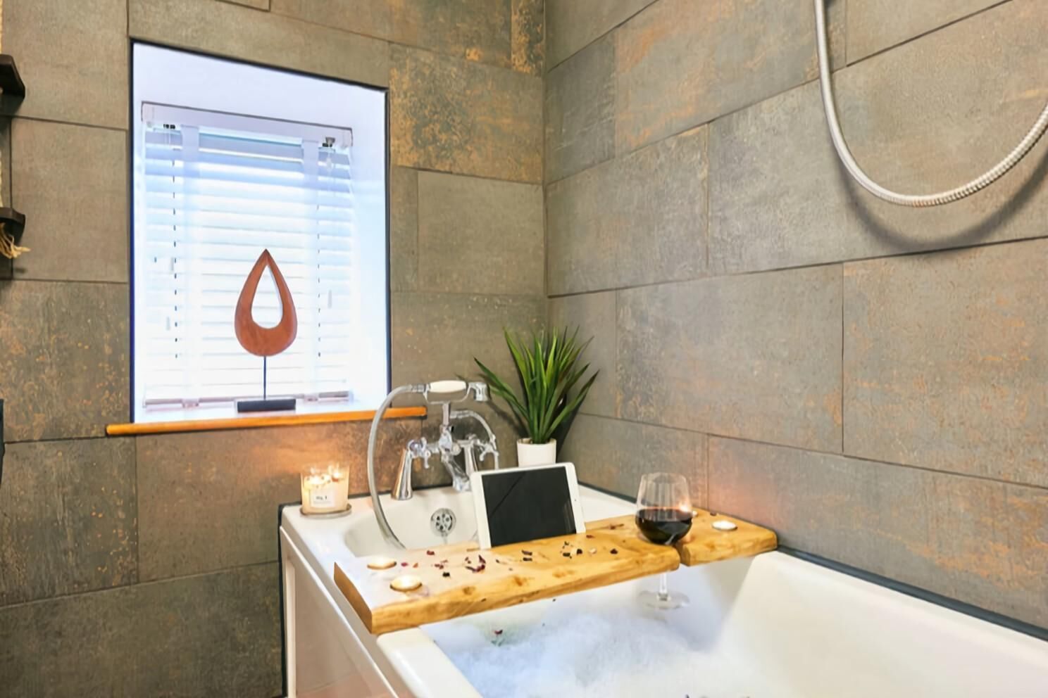 Un baño moderno con una bañera, una bandeja de madera con una copa de vino, una vela y una planta.