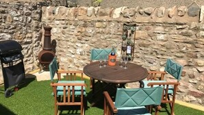 Terrassa exterior amb taula rodona, quatre cadires, una barbacoa i una paret de pedra.