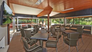 An outdoor dining area with wooden ceiling and large windows offering views of greenery. - Mobilehome with air conditioning, terrace and pool (Baia Domizia)