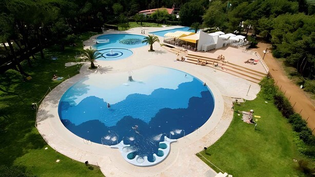 A large circular pool with a central fountain, surrounded by a grassy area and a few trees. - Mobilehome with air conditioning, terrace and pool (Baia Domizia)