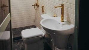 Ein Badezimmer mit weißen Fliesen im U-Bahn-Stil, einem goldfarbenen Duschkopf, einer weißen Toilette und einem weißen Waschbecken mit goldfarbenem Wasserhahn.