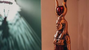 Eine Statue mit goldenem Kopf und roter Kopfbedeckung in einem Raum mit einer grünlich leuchtenden Lampe.