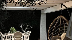 Une terrasse extérieure avec une table ronde et des chaises, un fauteuil suspendu et une plante en pot.