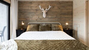 Ein Schlafzimmer mit einem hölzernen Kopfteil, einem großen Bett mit gesteppter Bettdecke, zwei Nachttischlampen und einem aufgehängten Hirschkopf an der Wand.
