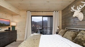 Ein Schlafzimmer mit einem Bett, einem Schminktisch, einem aufgehängten Hirschgeweih und einem großen Fenster mit Vorhängen.