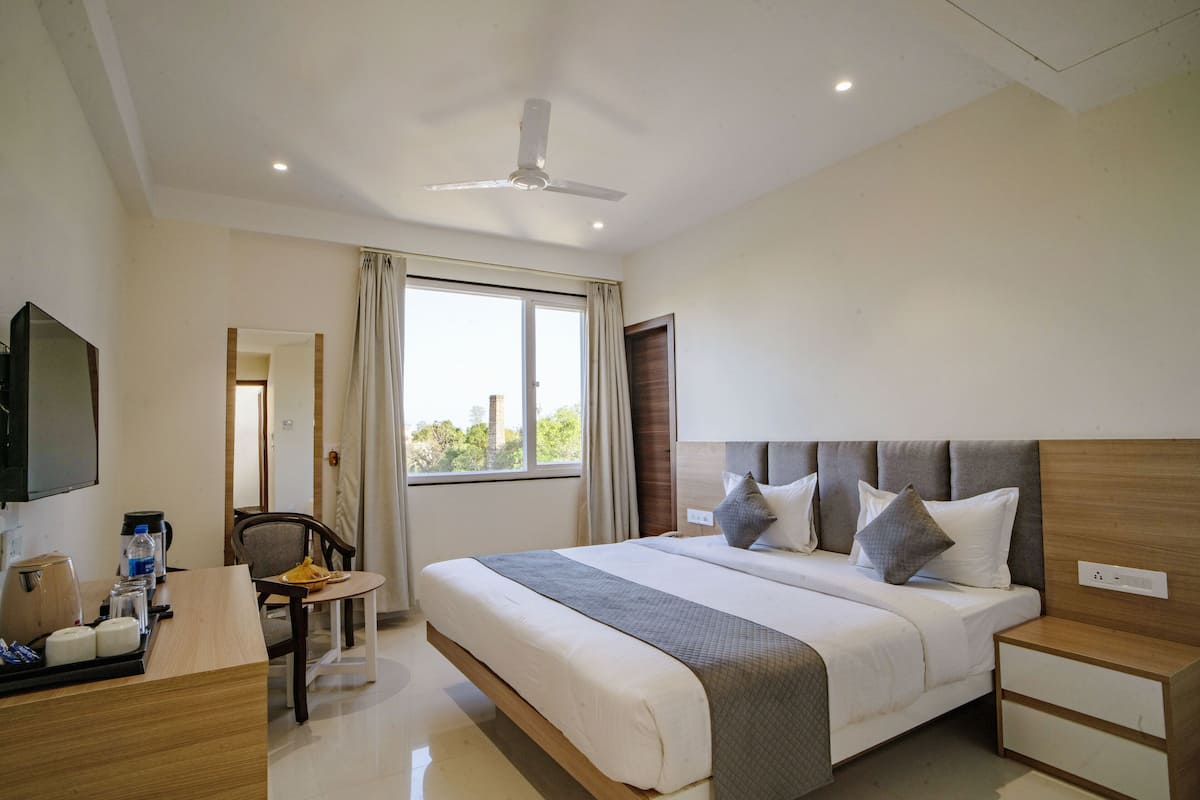A hotel room with a large bed, bedside tables, a desk with a chair, a television, and a window with curtains.