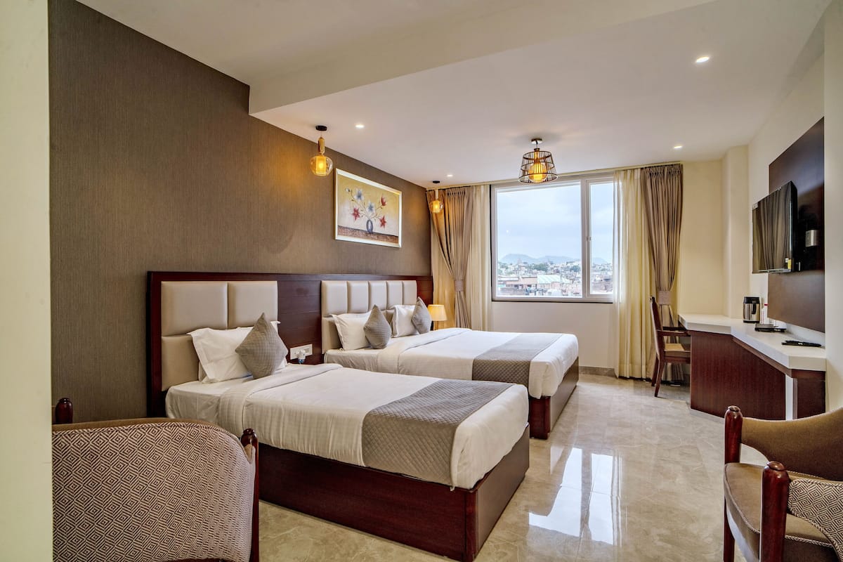 A hotel room with two beds, a desk, a chair, a TV, and a window with a city view.