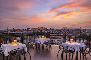 Una terraza con mesas preparadas para comer, con vistas a un paisaje urbano al atardecer.