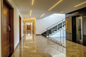Un pasillo moderno de hotel con un suelo de mármol pulido, una escalera con barandillas de cristal y puertas de madera.