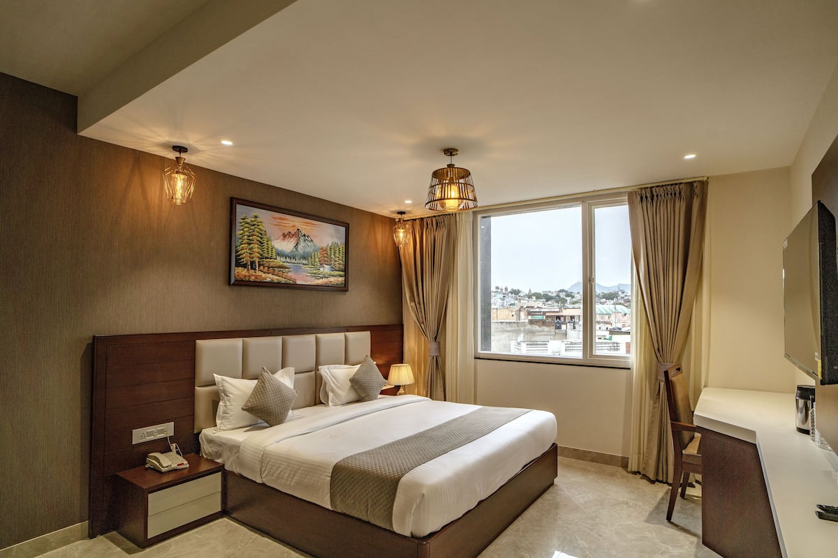 A hotel room with a large bed, a desk, a TV, and a window with curtains.