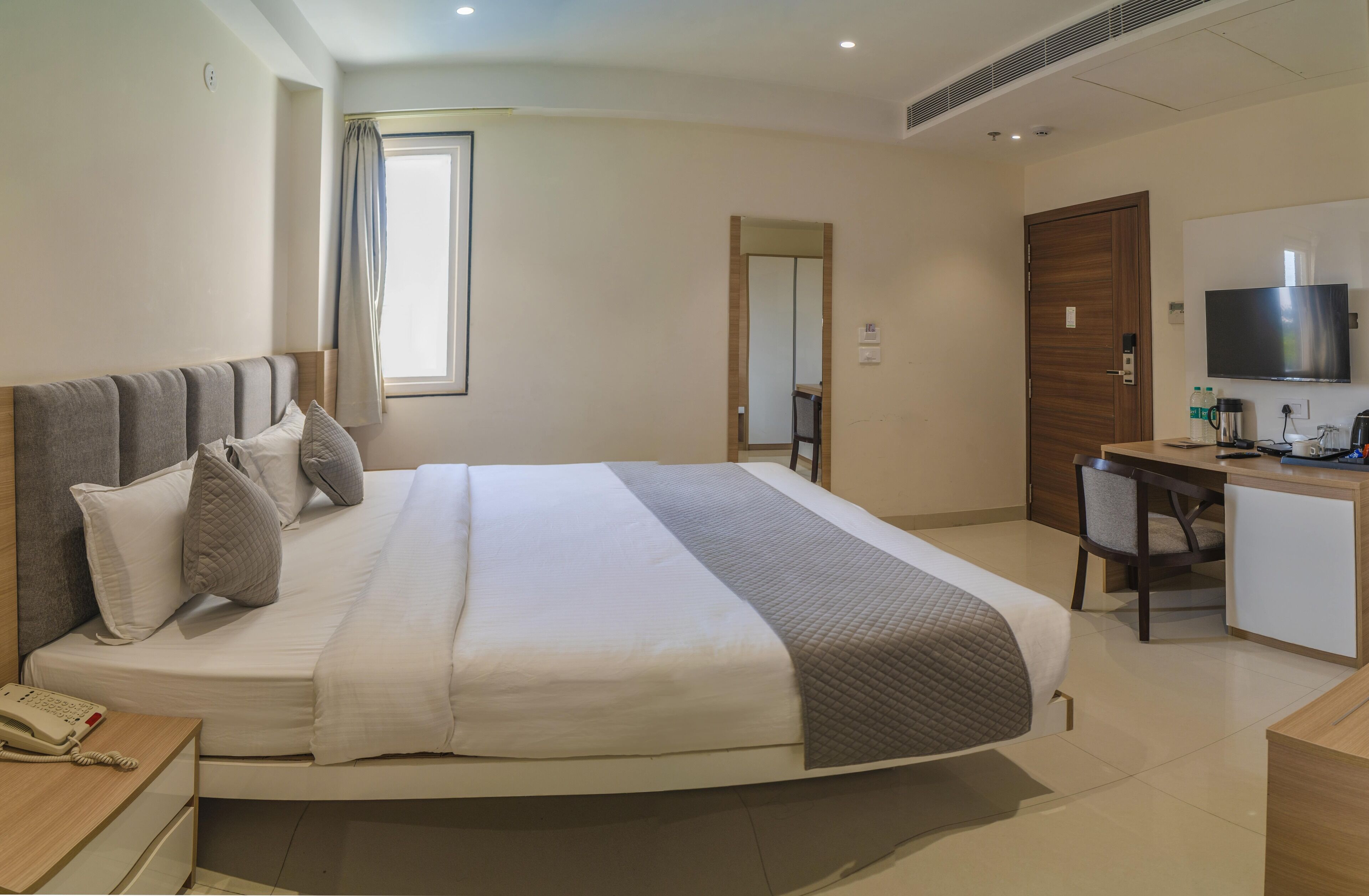 A hotel room with a bed, bedside table, desk, chair, TV, and a window with curtains.