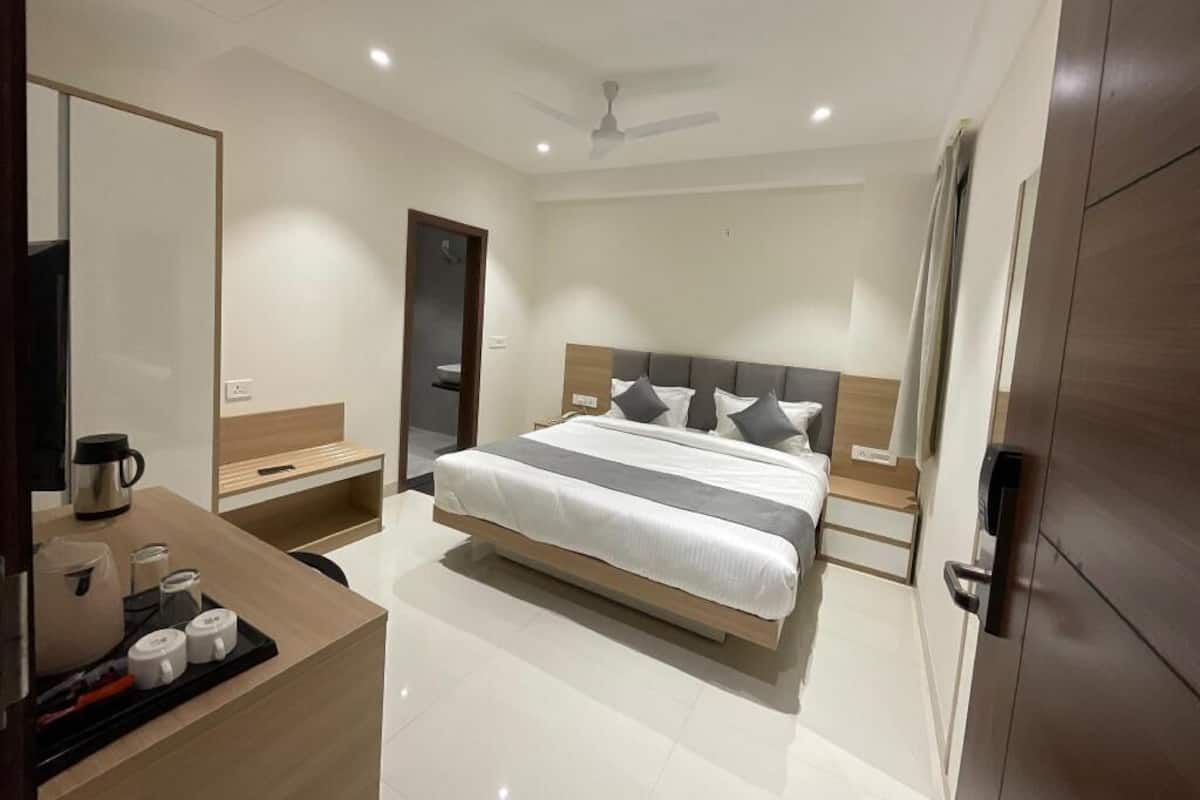 A modern hotel room with a bed, bedside tables, a desk with a coffee maker, and a mirror.