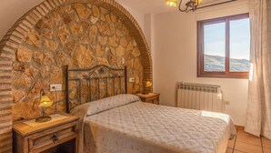 Ein Schlafzimmer mit Steinbogen, einem hölzernen Bett, einem Nachttisch mit Lampe, einer Heizung und einem Fenster mit Blick.
