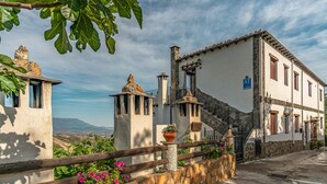 Ein traditionelles Gebäude mit einer steinernen Fassade, einer Treppe, die zum Eingang führt, und Blick auf die umliegende Landschaft.