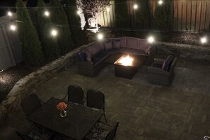 A patio with a fire pit, seating area, and string lights.
