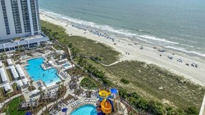 Ett semesterhotell med ett stort poolområde, en vattenrutschkana och en strand med parasoller.