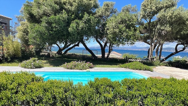 A swimming pool surrounded by lush greenery and trees, with a view of the sea in the background. - Villa 130 m2, pool and terrace, facing the sea, on 1300m2 of wooded grounds. (Hyères)
