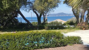 A deck with two white lounge chairs facing a landscaped garden and a view of the sea. - Villa 130 m2, pool and terrace, facing the sea, on 1300m2 of wooded grounds. (Hyères)