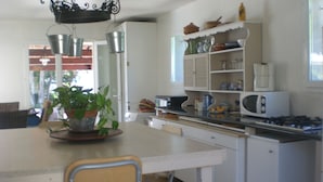 A compact kitchen with a dining table, chairs, a microwave, and a gas stove. - Villa 130 m2, pool and terrace, facing the sea, on 1300m2 of wooded grounds. (Hyères)
