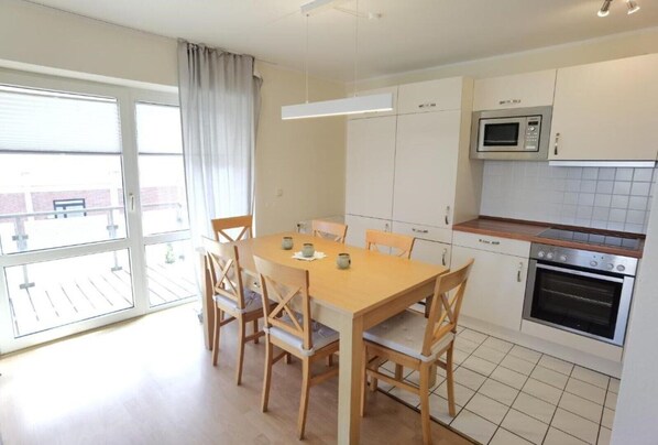 A modern kitchen with a dining table and chairs, a microwave, oven, and a view of the outside. - Schaake Schillig near the beach (Wangerland)