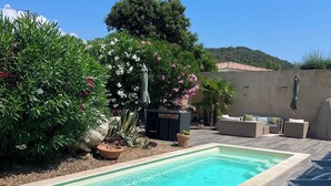 A rectangular swimming pool with clear blue water, surrounded by a wooden deck. There are lounge chairs and a small seating area with a table and chairs. - Villa Avec Piscine (Porto-Vecchio)