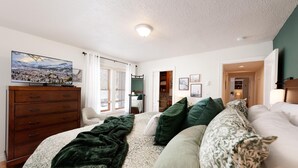 A bedroom with a bed, a dresser, a chair, and a television on the wall. - The Passport Suite | Downtown Access, Pool/Hot Tub, Near FLC, Trails & Golf (Durango)