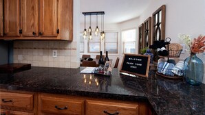 A kitchen with wooden cabinets, a marble countertop, and a welcome sign. - The Passport Suite | Downtown Access, Pool/Hot Tub, Near FLC, Trails & Golf (Durango)