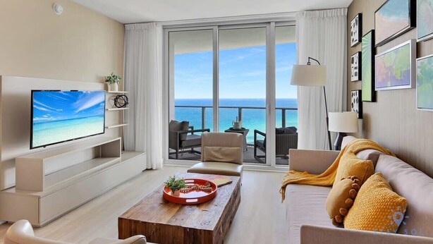 Una camera d'albergo moderna con una grande TV, un tavolino in legno, un divano e un balcone con vista sul mare.