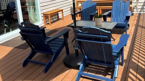An outdoor deck with blue Adirondack chairs, a wooden table, and a beige umbrella.
