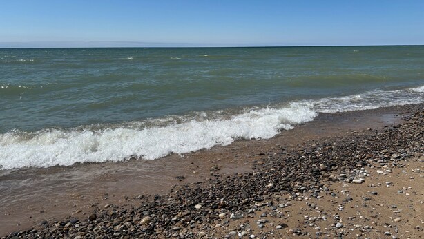 A beach with a pebbly shore and calm waves.